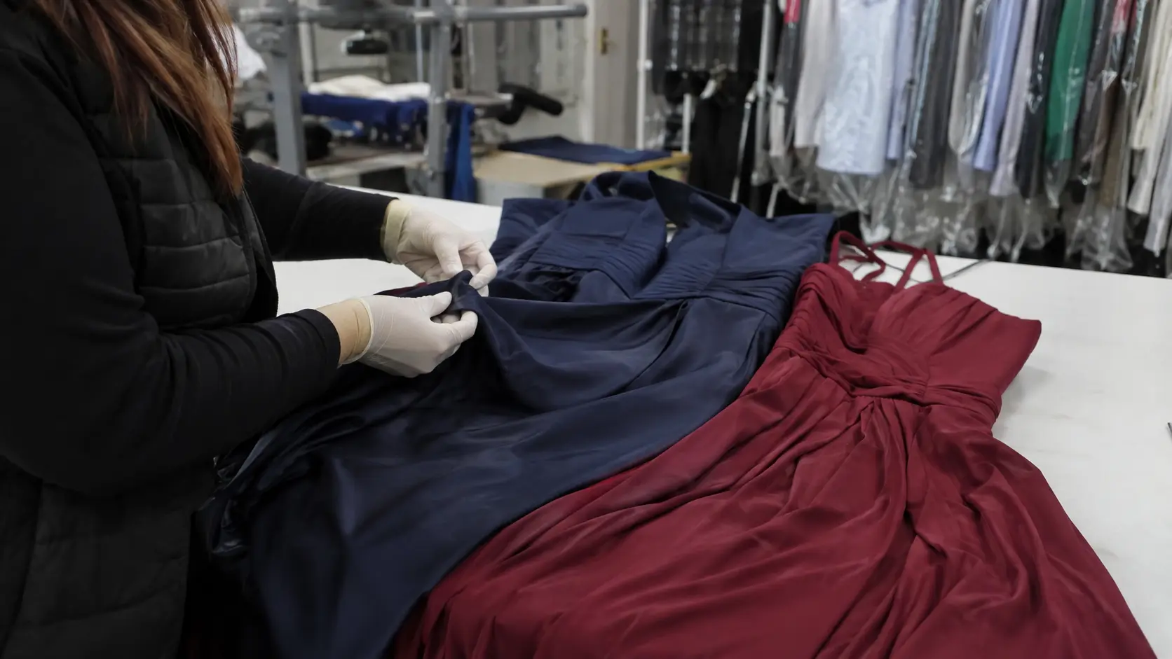 Operaria revisando dos vestidos de fiesta sobre una mesa de trabajo en una tintorería de Lorca